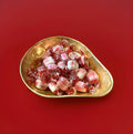 Individually wrapped pink and white coloured sweets with an icing outer shell and a soft caramel centre in a gold bowl on a red background 