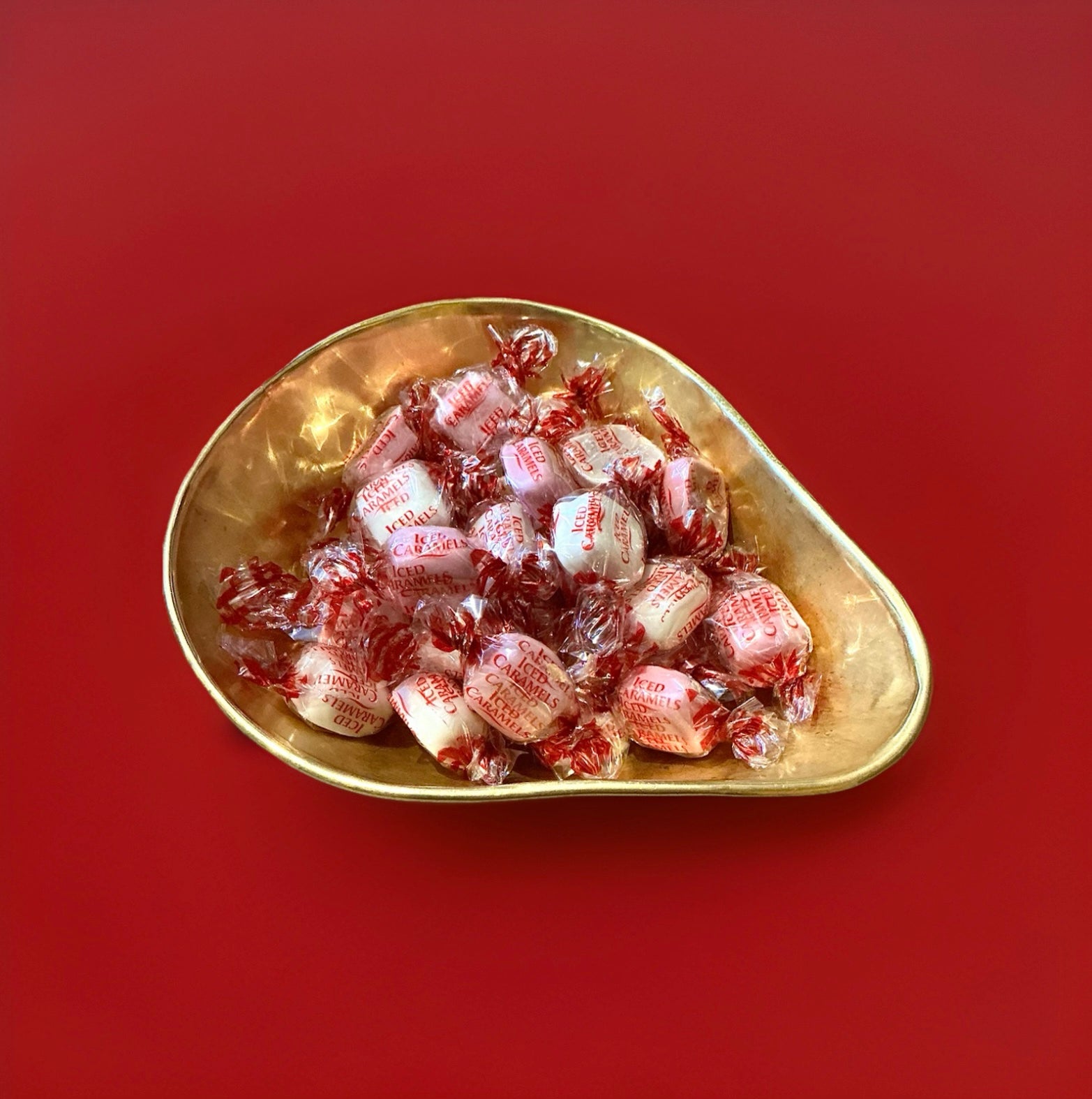 Individually wrapped pink and white coloured sweets with an icing outer shell and a soft caramel centre in a gold bowl on a red background 