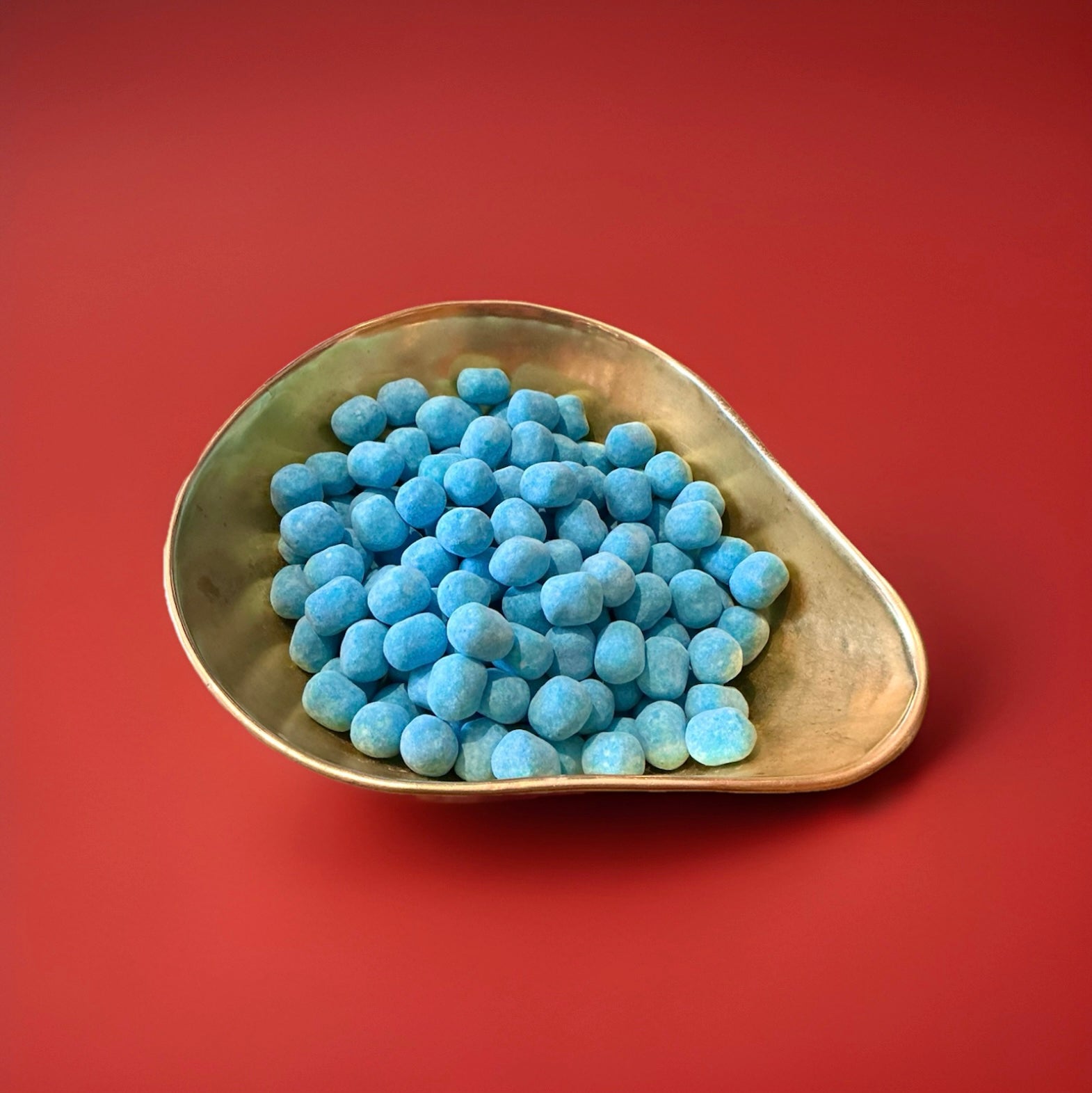 Round shaped blue coloured blue Raspberry flavoured Bon Bon’s in a gold bowl on a red background 