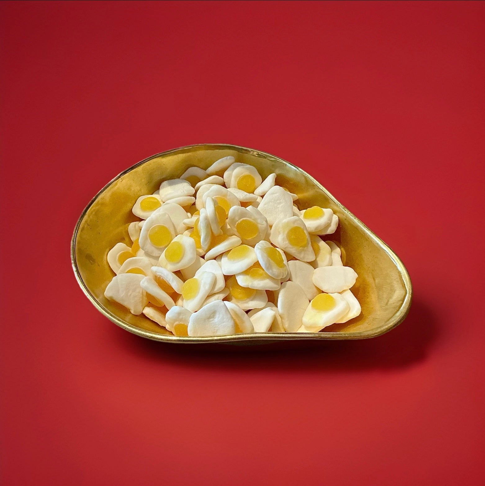 White an yellow fried egg jelly sweets in a gold bowl on a red background 