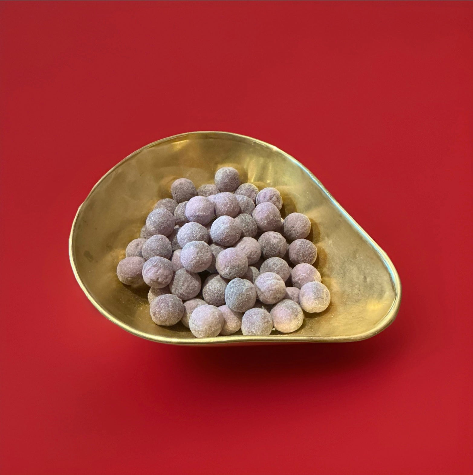 Dark and light purple round hard boiled sweet with a fizzy dandelion and burdock flavour in a gold bowl with a red background 