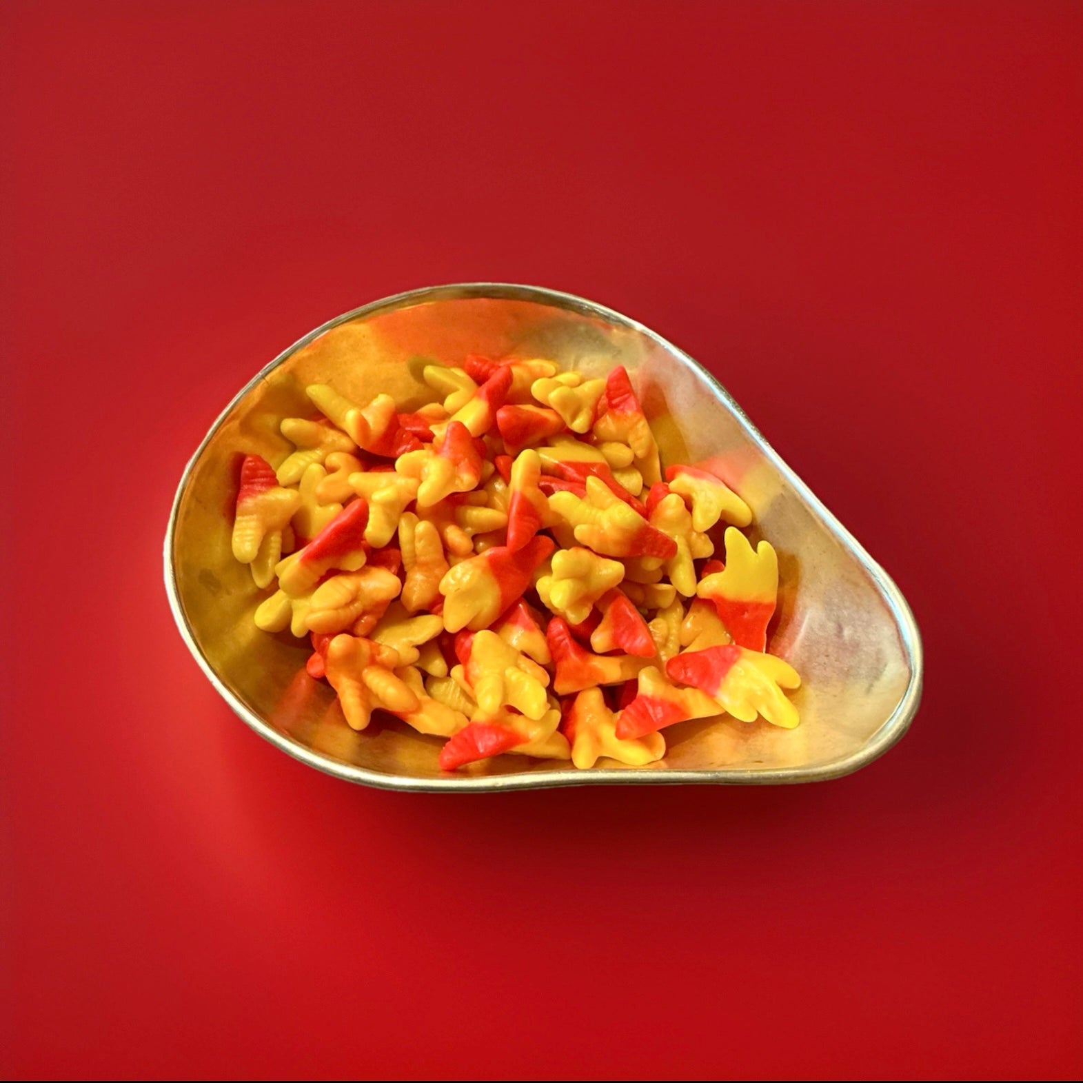 Red and yellow coloured jelly sweets in the shape of chickens feet in a gold bowl on a red background 