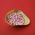 Round shaped pink coloured strawberry flavoured Bon Bon’s in a gold bowl on a red background 