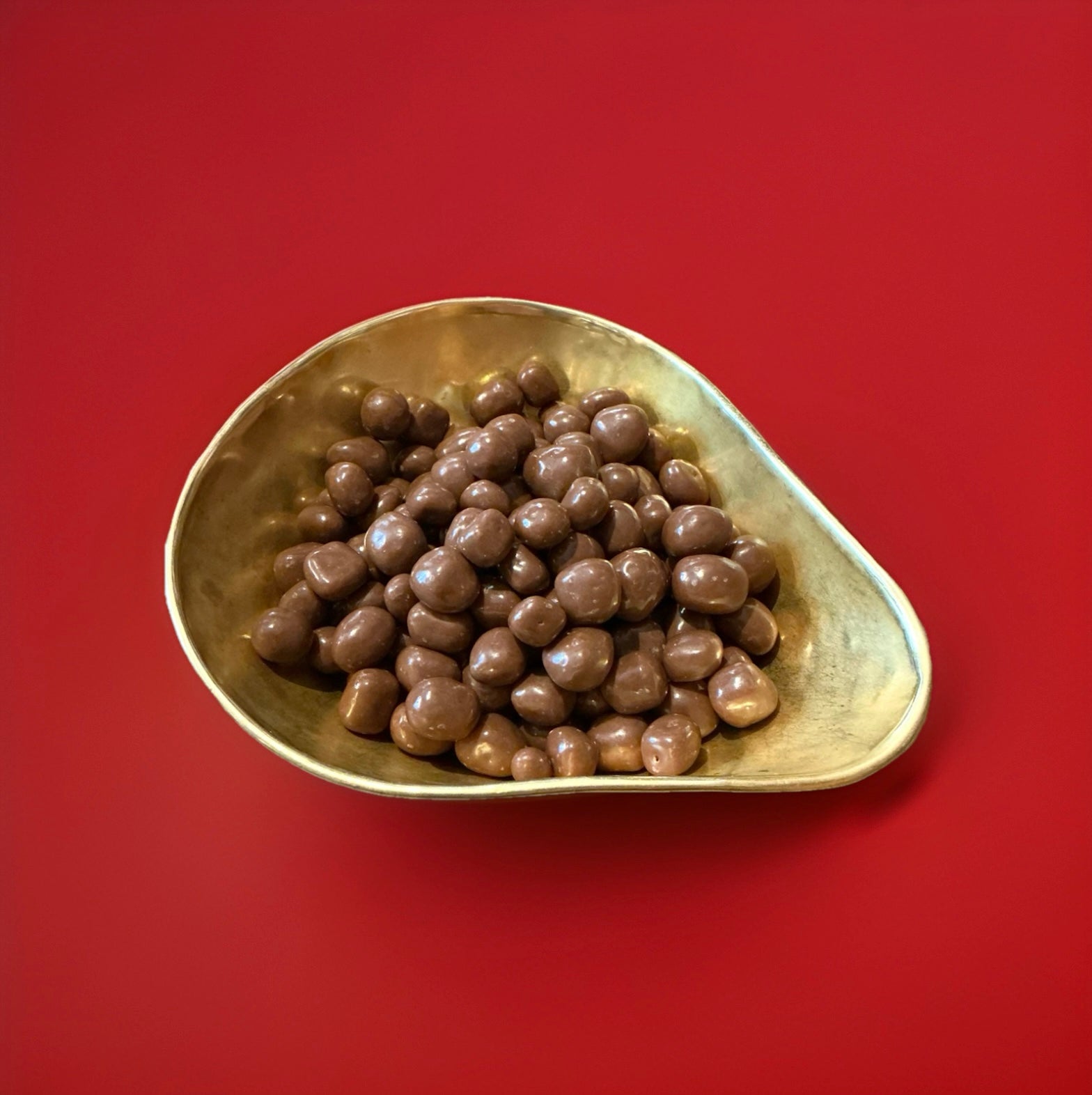 Bite sized pieces of candied ginger coated in milk chocolate in a gold bowl on a red background 