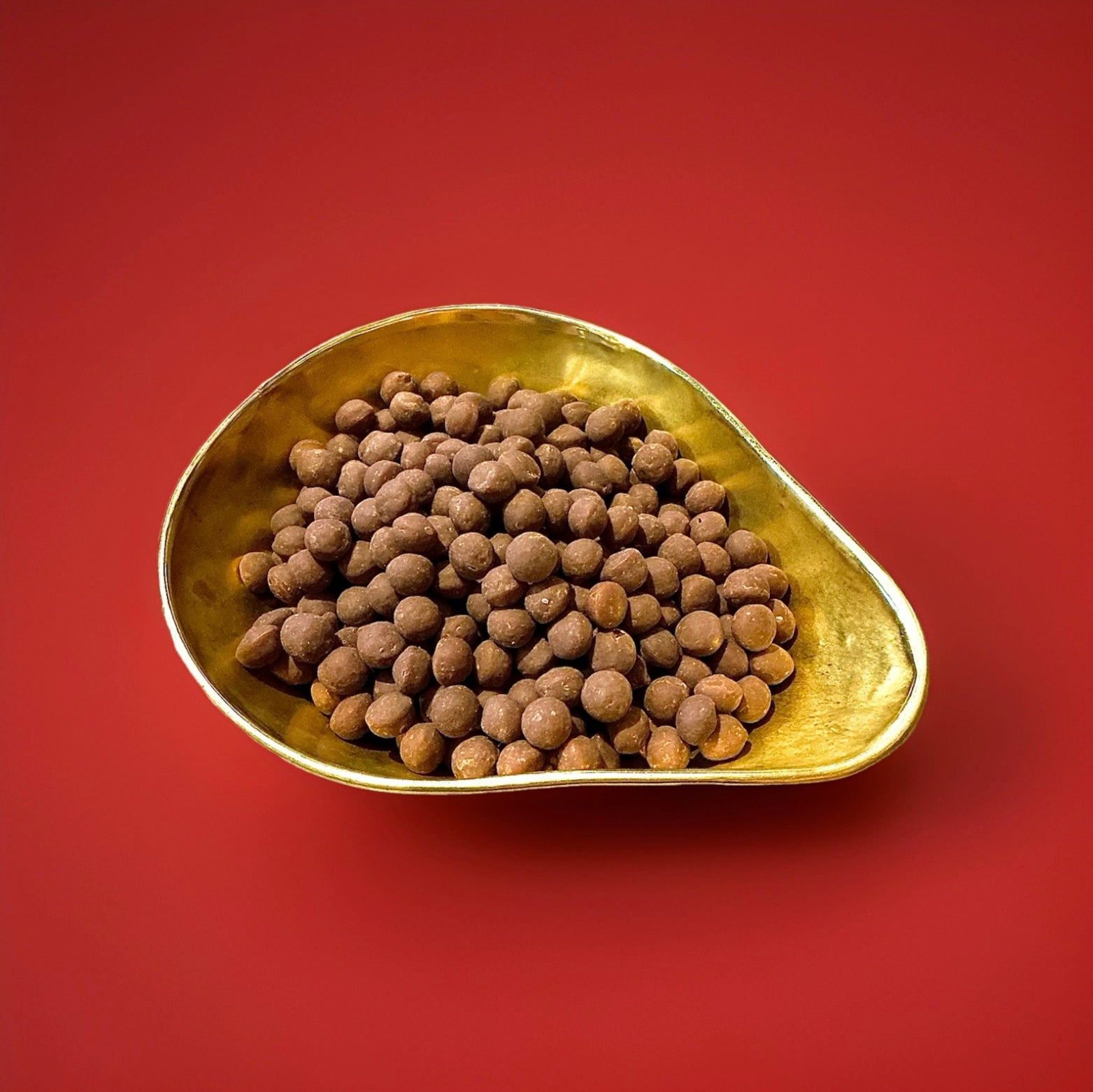 Chewing nuts a ball of toffee wrapped in milk chocolate in a gold bowl with a red background 