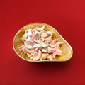 Milk flavoured pink and white gummy sweets in the shape of teeth in a gold bowl on a red background 