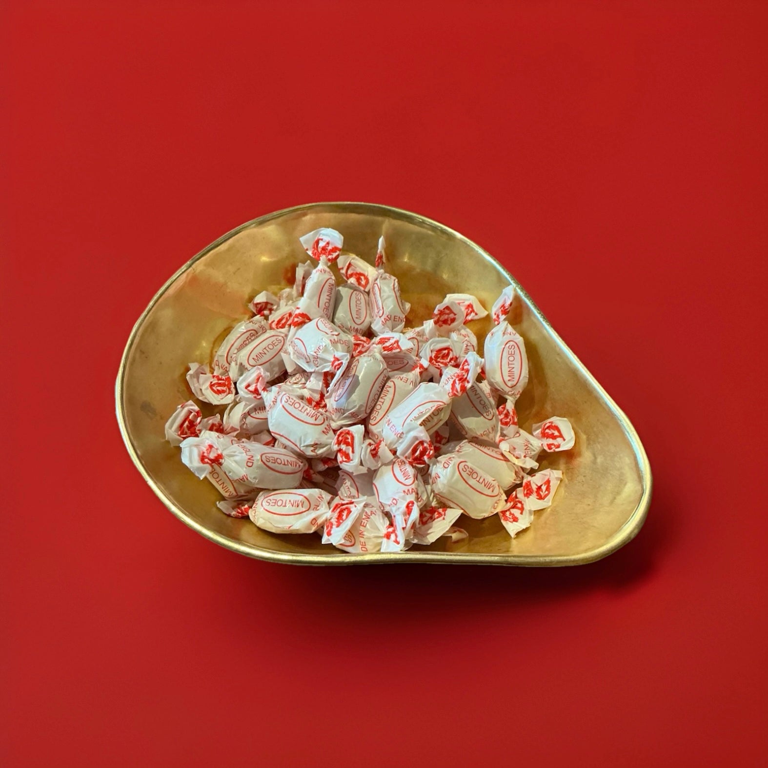 Individually wrapped Mintoes butter mints in a gold bowl on a red background 