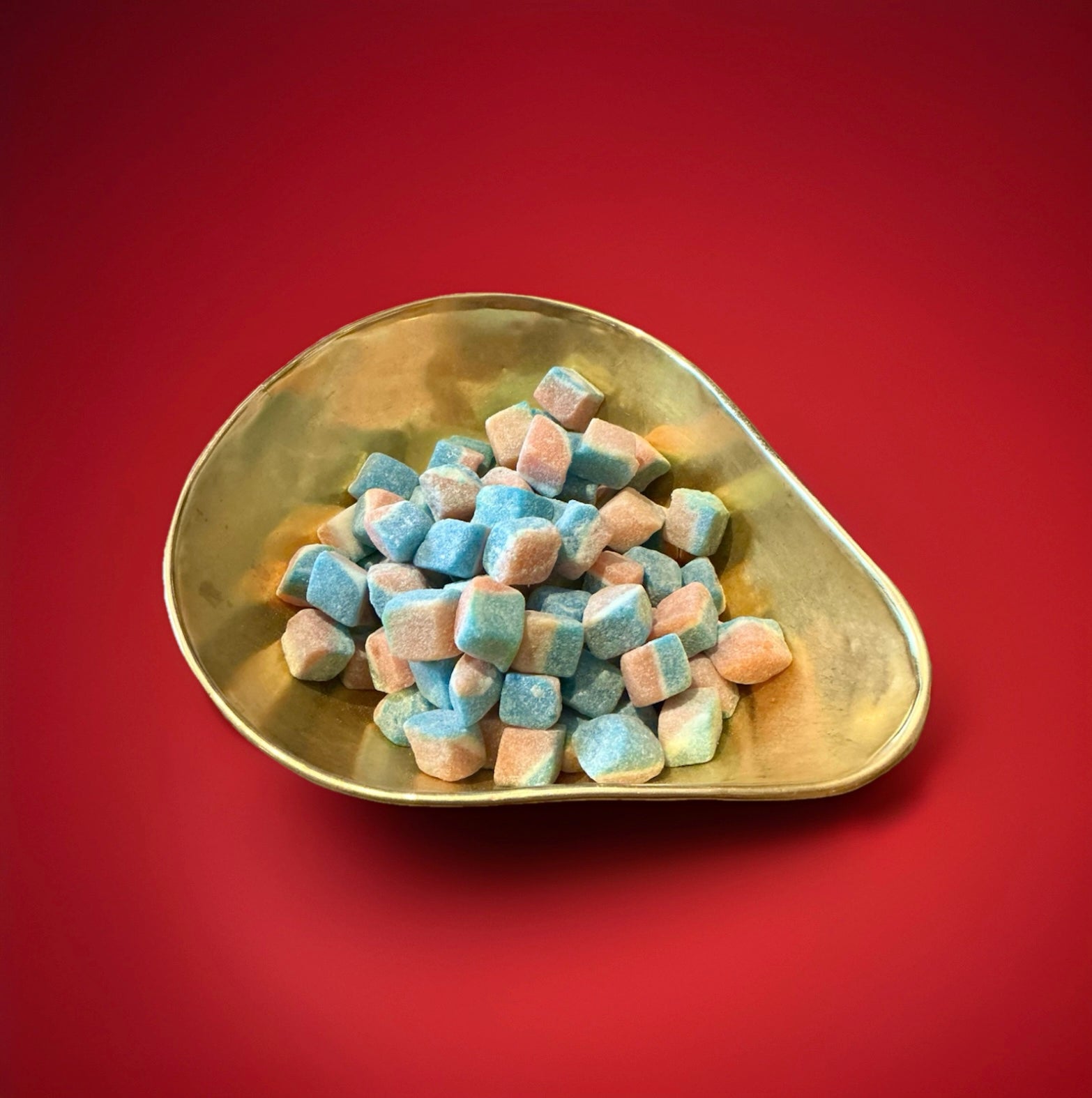 Orange white and blue hard boiled bite sized cubes with an iron brew flavour in a gold bowl with a red background 