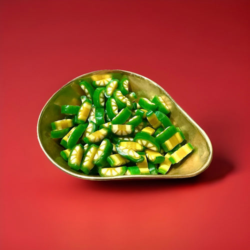 Green and yellow lemon and lime sweets in a gold bowl with a red background 