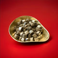 Gold and brown bite size rock cuttings with a ginger flavour in a gold bowl with a red background 