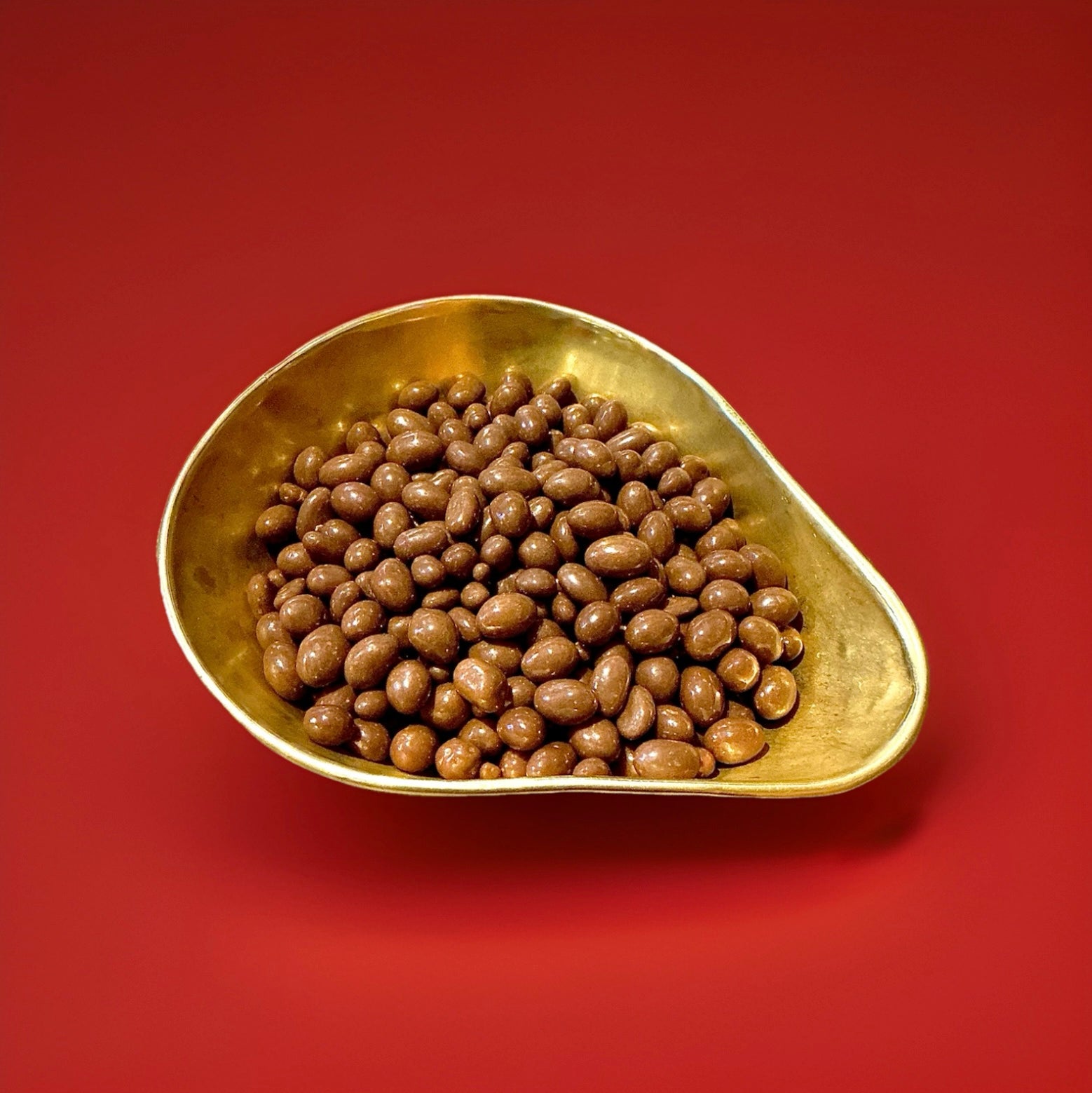 Milk chocolate covered peanuts in a gold bowl on a red background 