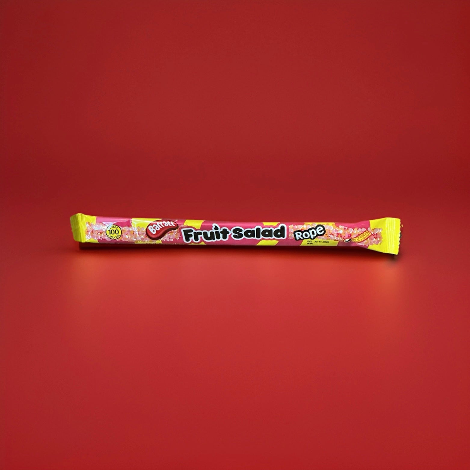 Wrapped long fruit salad flavoured jelly sweet with sprinkles on in a yellow and pink wrapper 