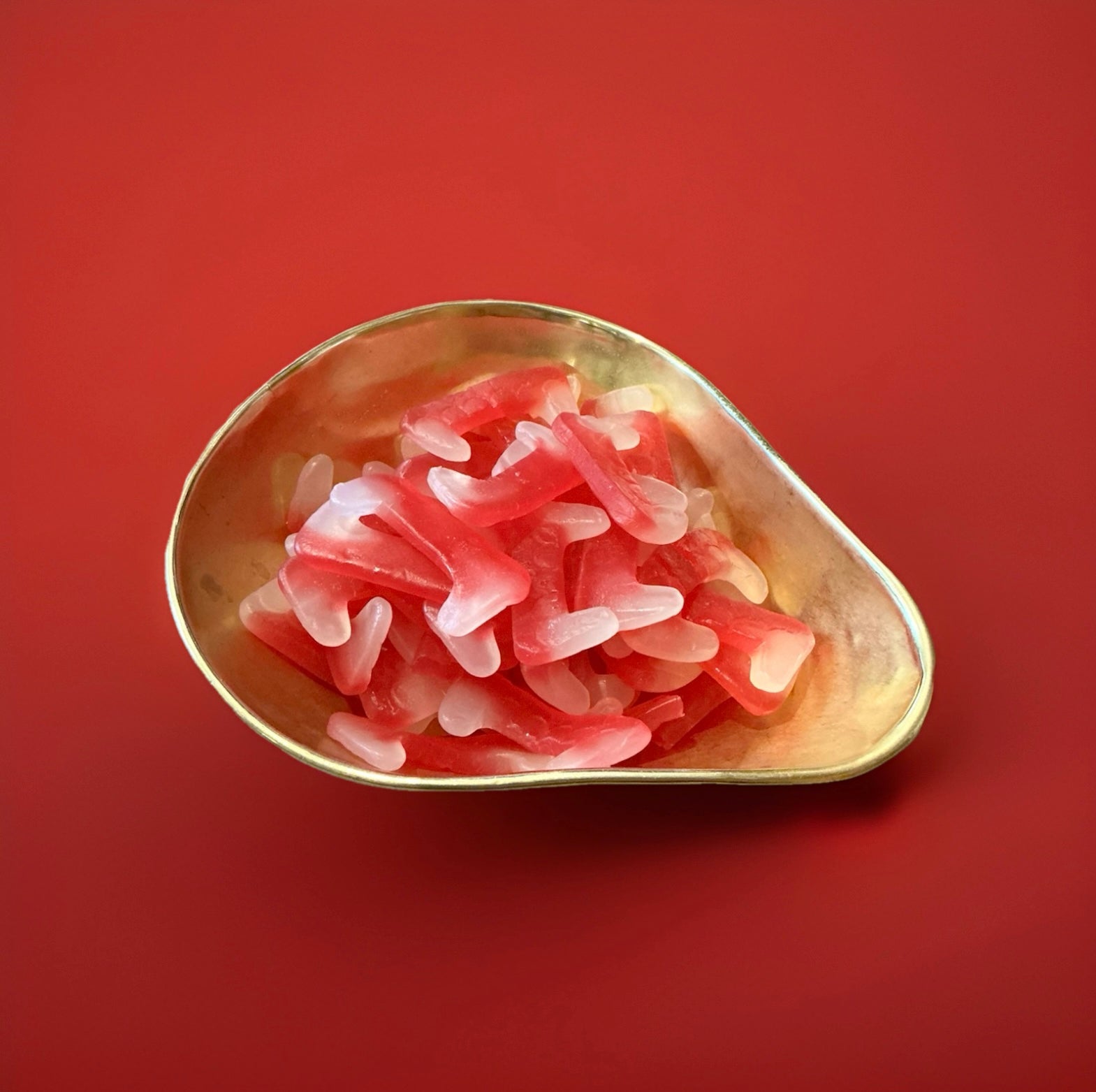 Fang shaped red and white coloured gummy jelly sweets with a fruit flavour in a gold bowl on a red background 