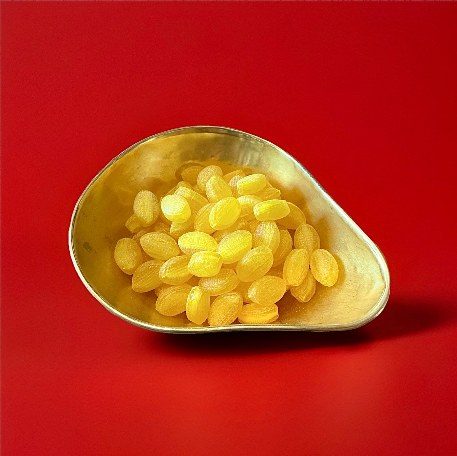 Yellow lemon flavoured and shaped hard boiled sweets with a sherbet centre in a gold bowl with a red background 