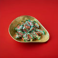 Individually wrapped spearmint chews in red white and green wrappers in a gold bowl on a red background 