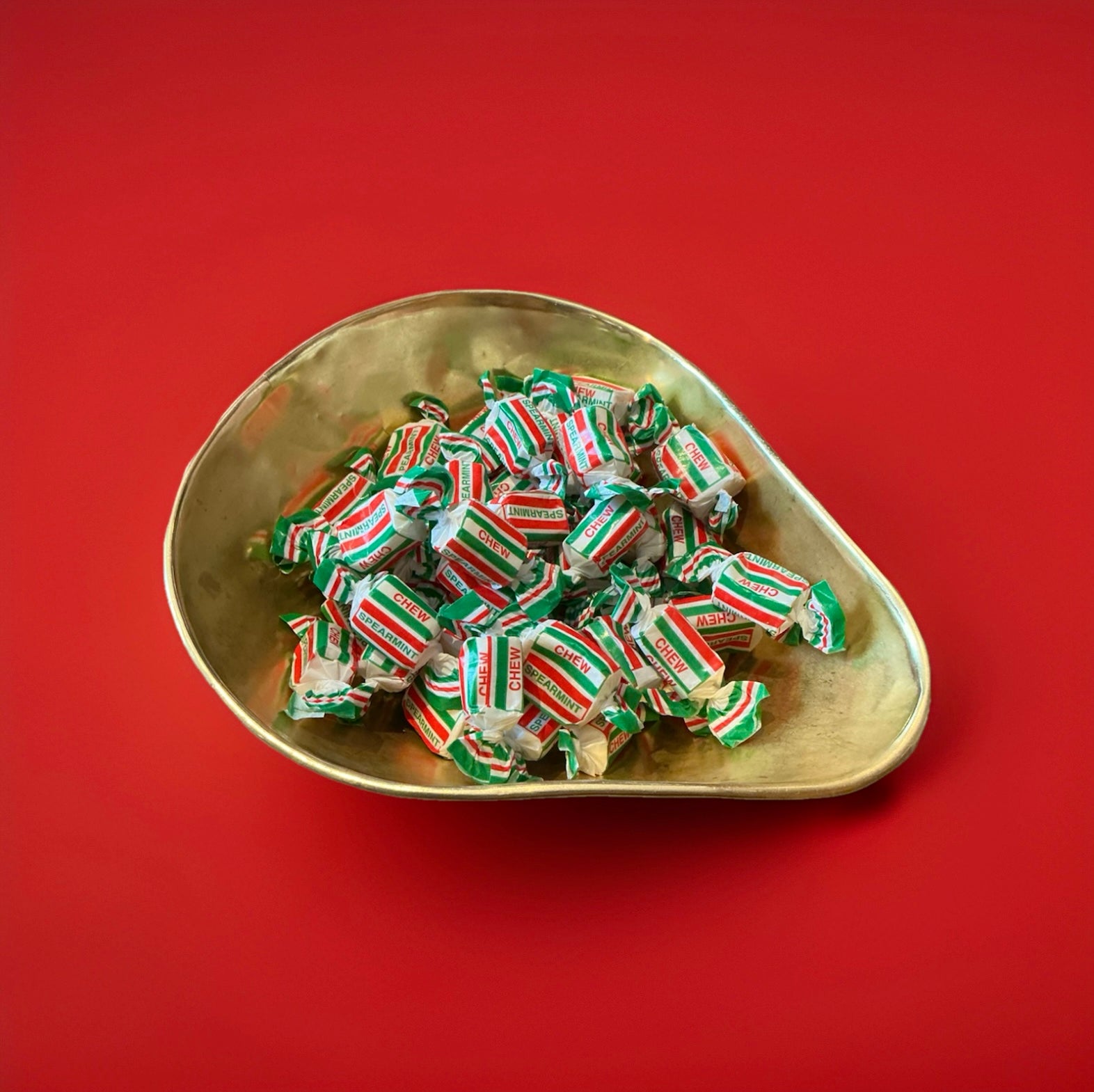 Individually wrapped spearmint chews in red white and green wrappers in a gold bowl on a red background 