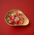 Red and Green coloured strawberry flavoured and shaped jelly sweets in a gold bowl on a red background 