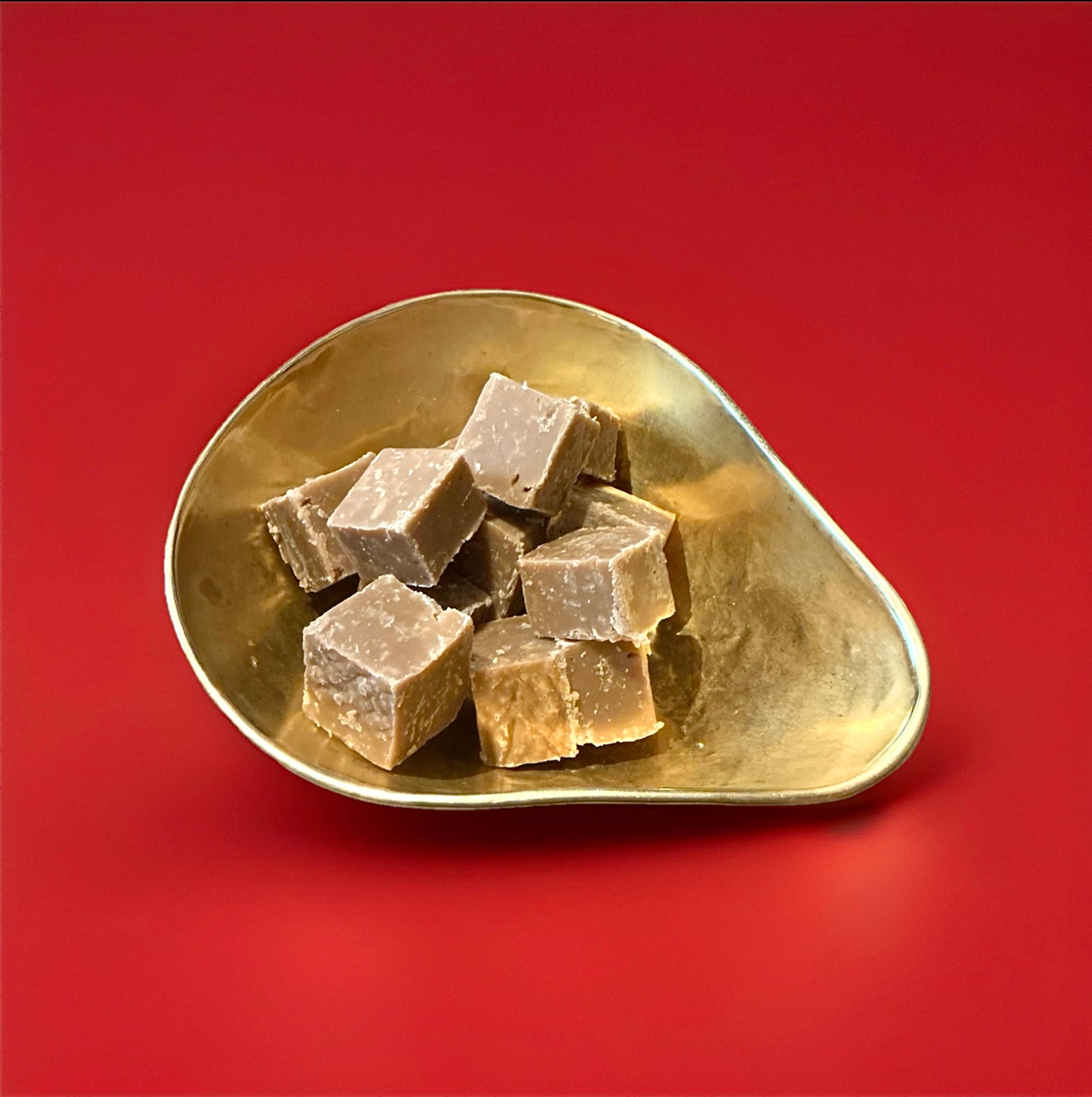 Large pieces of salted caramel fudge in a gold bowl with a red background 