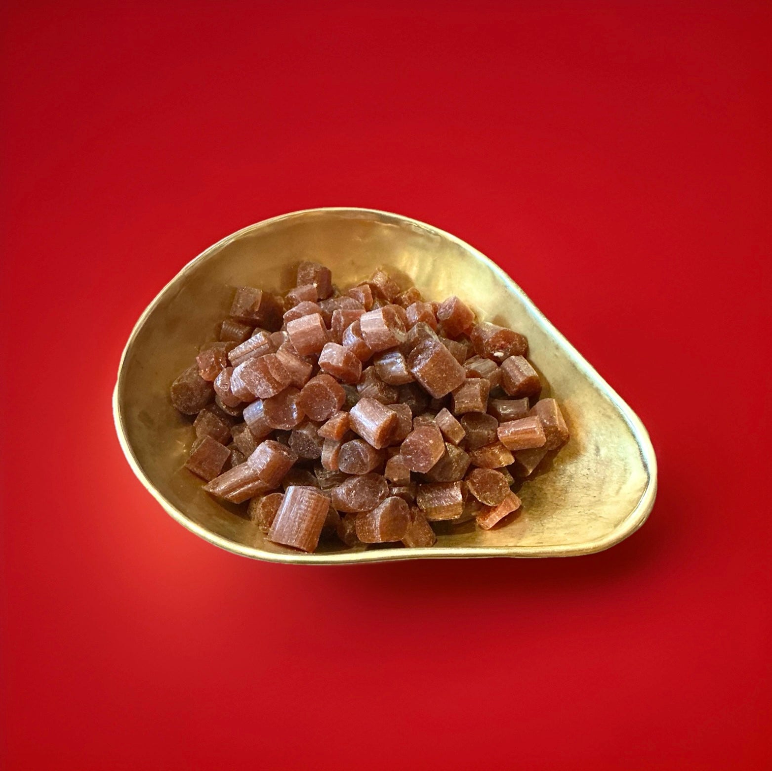 Brown coloured liquorice and root beer flavoured rock cuttings in a gold bowl with a red background 