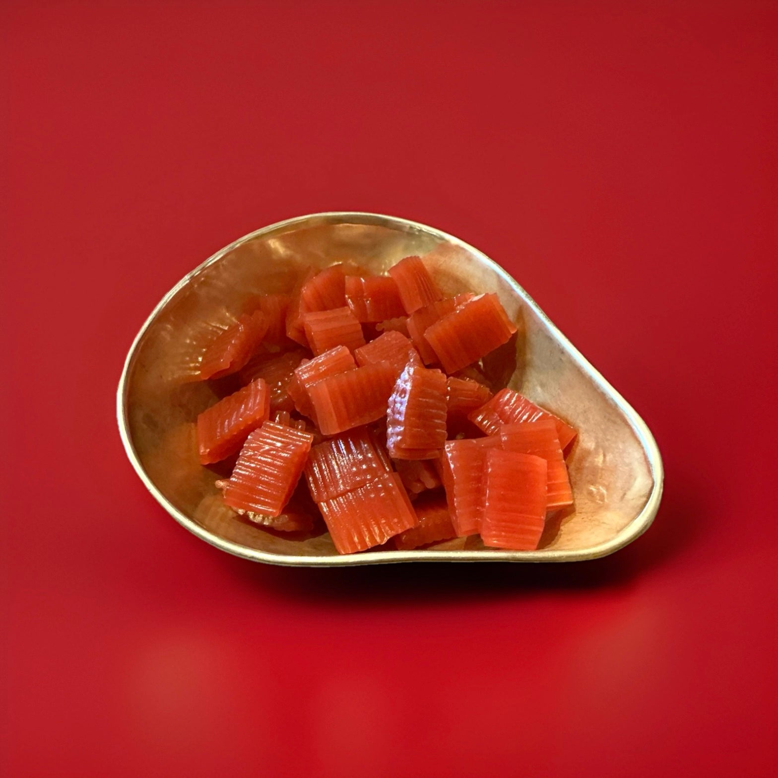 Strawberry flavoured red coloured soft liquorice blocks in a gold bowl on a red background 