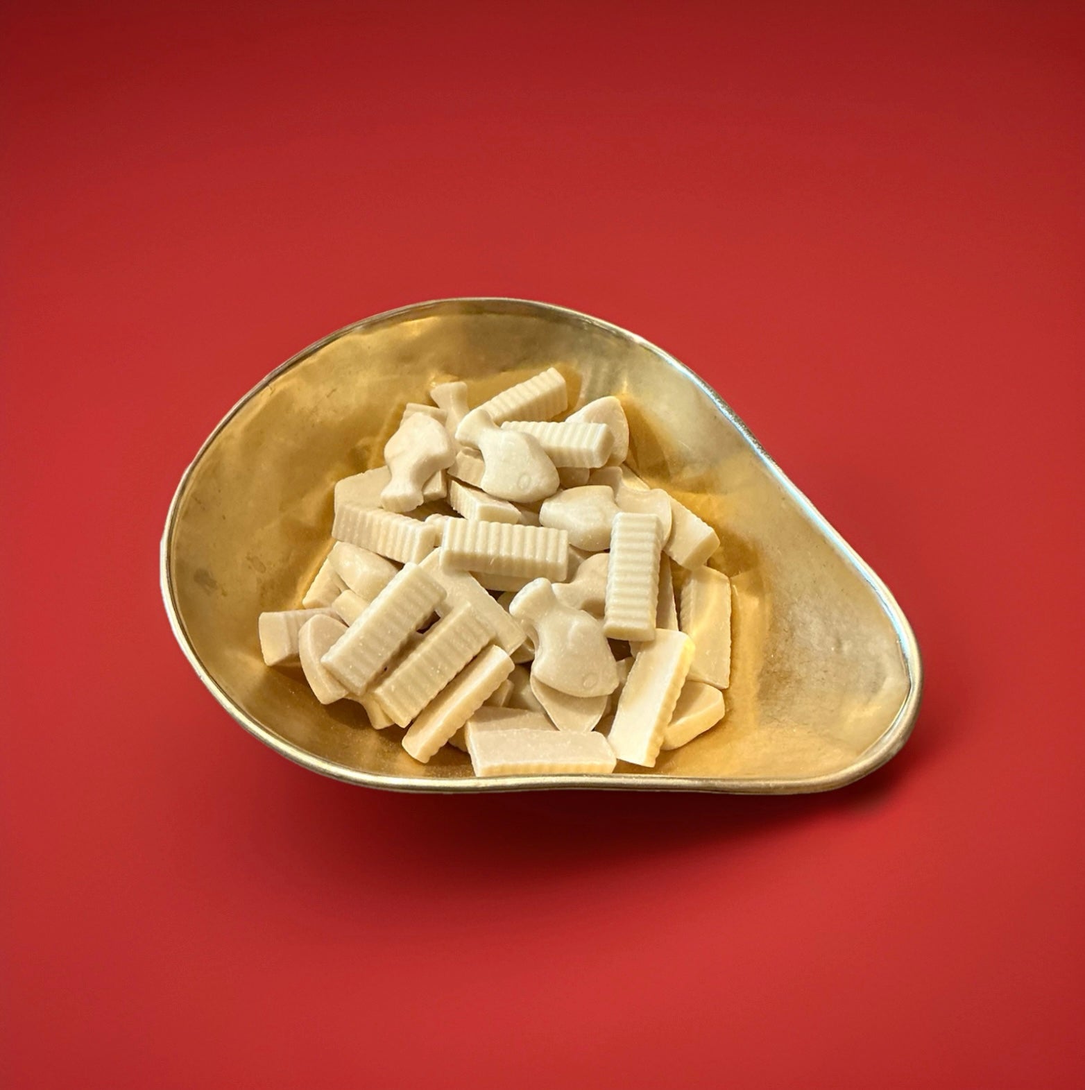 Fish and chip shaped white chocolate sweets in a gold bowl on a red background 