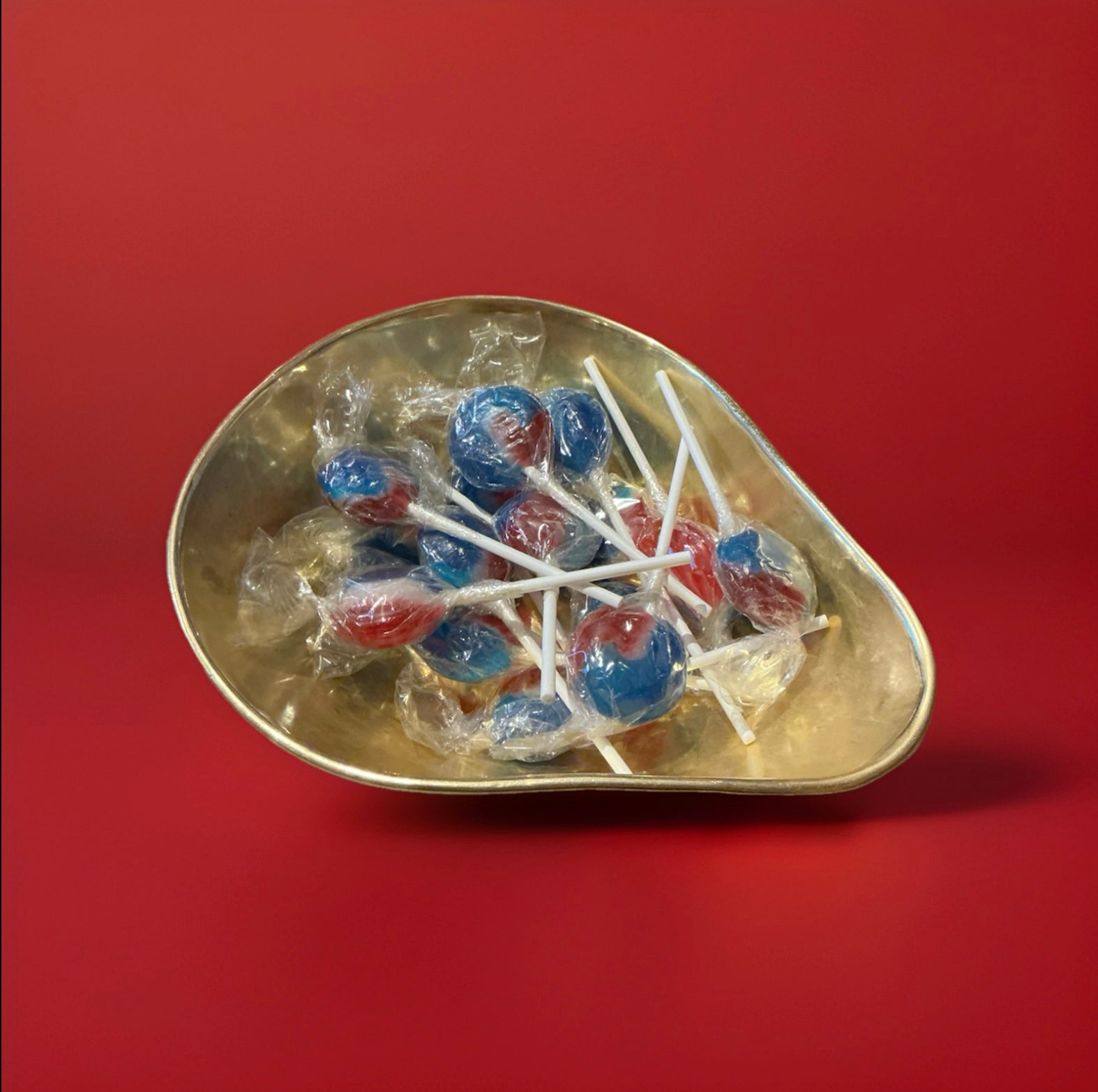 Individually wrapped hard boiled red white and blue mixed fruit flavoured lolly in a gold bowl on a red background 