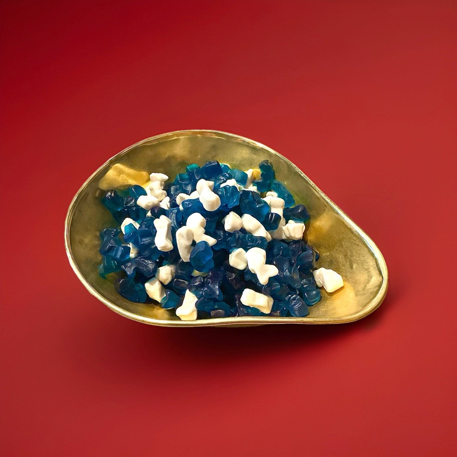 Blue and white dolphin shaped jelly sweets in a gold bowl on a red background 
