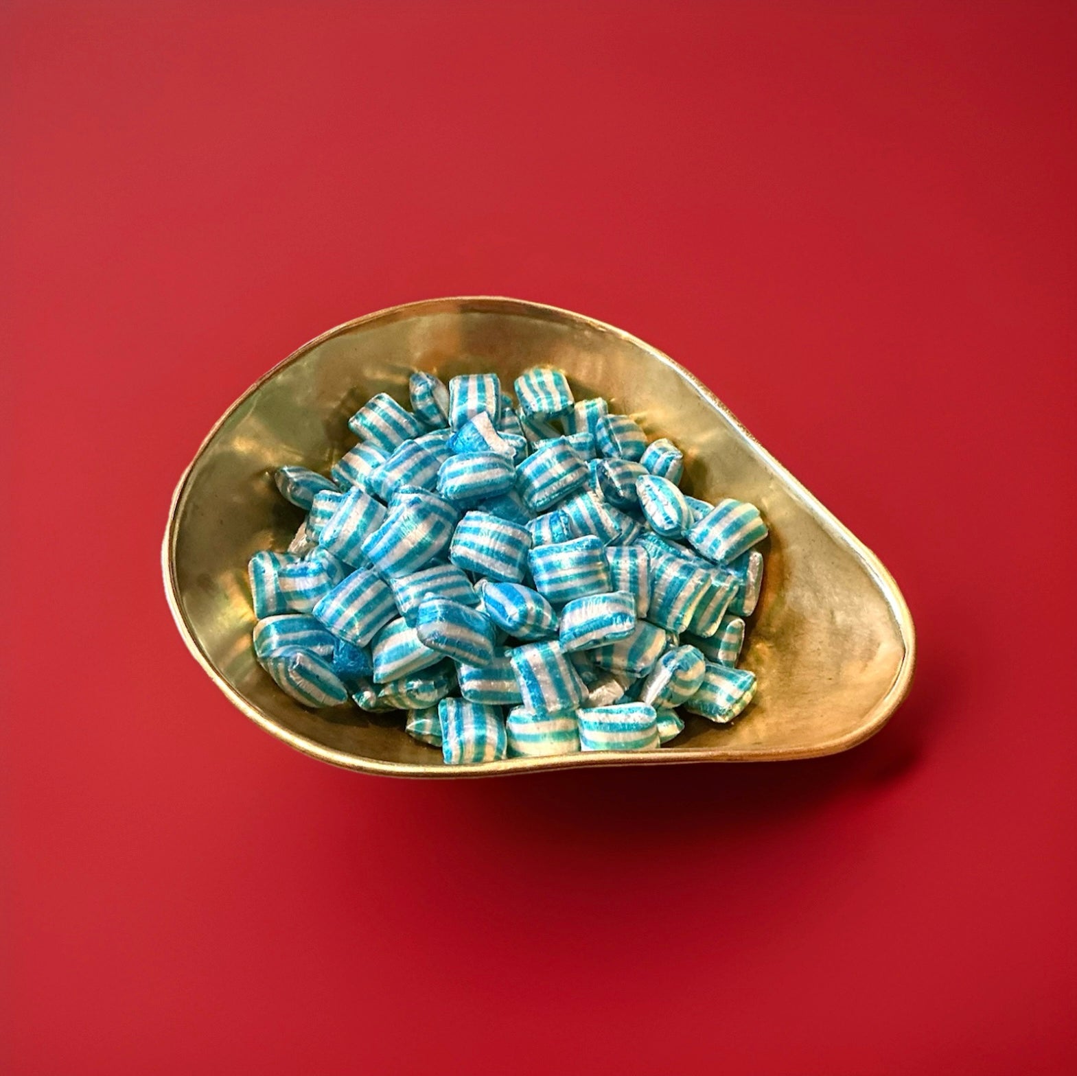 Blue and white striped cola flavoured hard boiled sweets in a gold bowl with a red background 