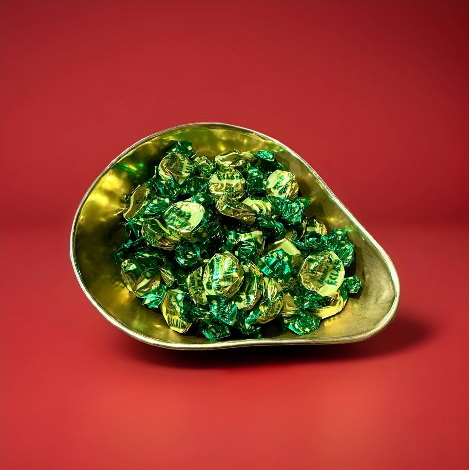 Individually wrapped banana flavoured toffee with a chocolate centre in a gold bowl on a red background 