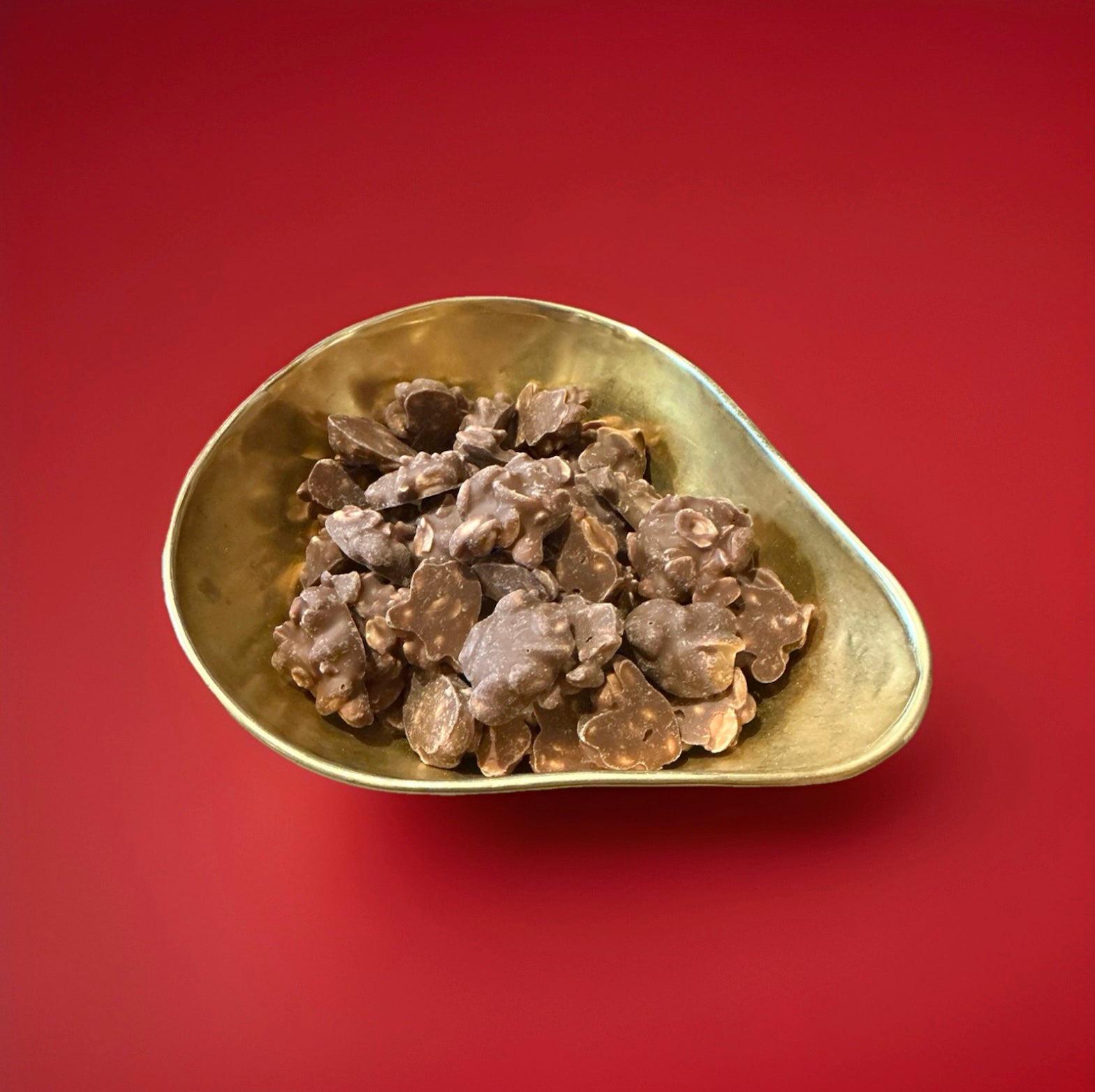Clusters of milk chocolate covered peanuts in a gold bowl on a red background 