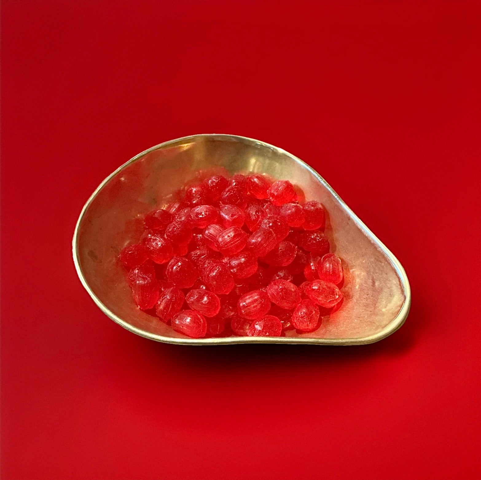 Monarch cherry drops are bright red hard boiled sweets in a gold bowl with a red background 