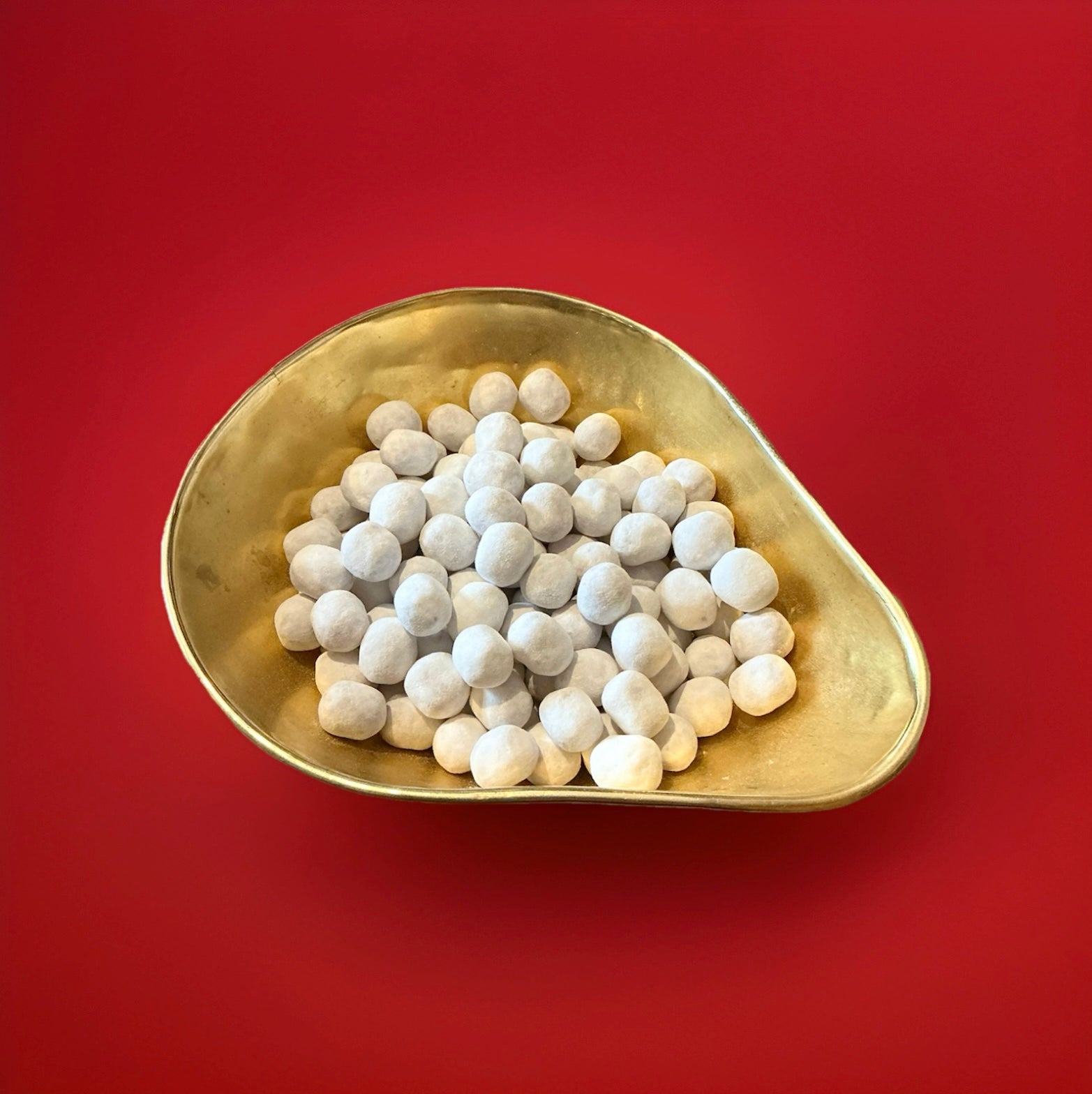 Round shaped white coloured toffee flavoured Bon Bon’s in a gold bowl on a red background 
