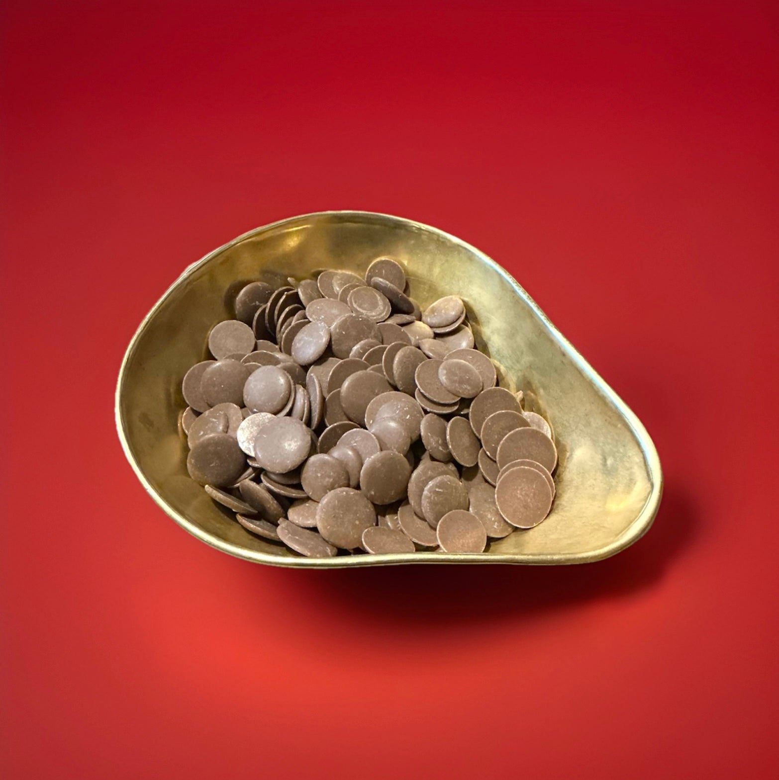 Milk chocolate buttons in a gold bowl on a red background 