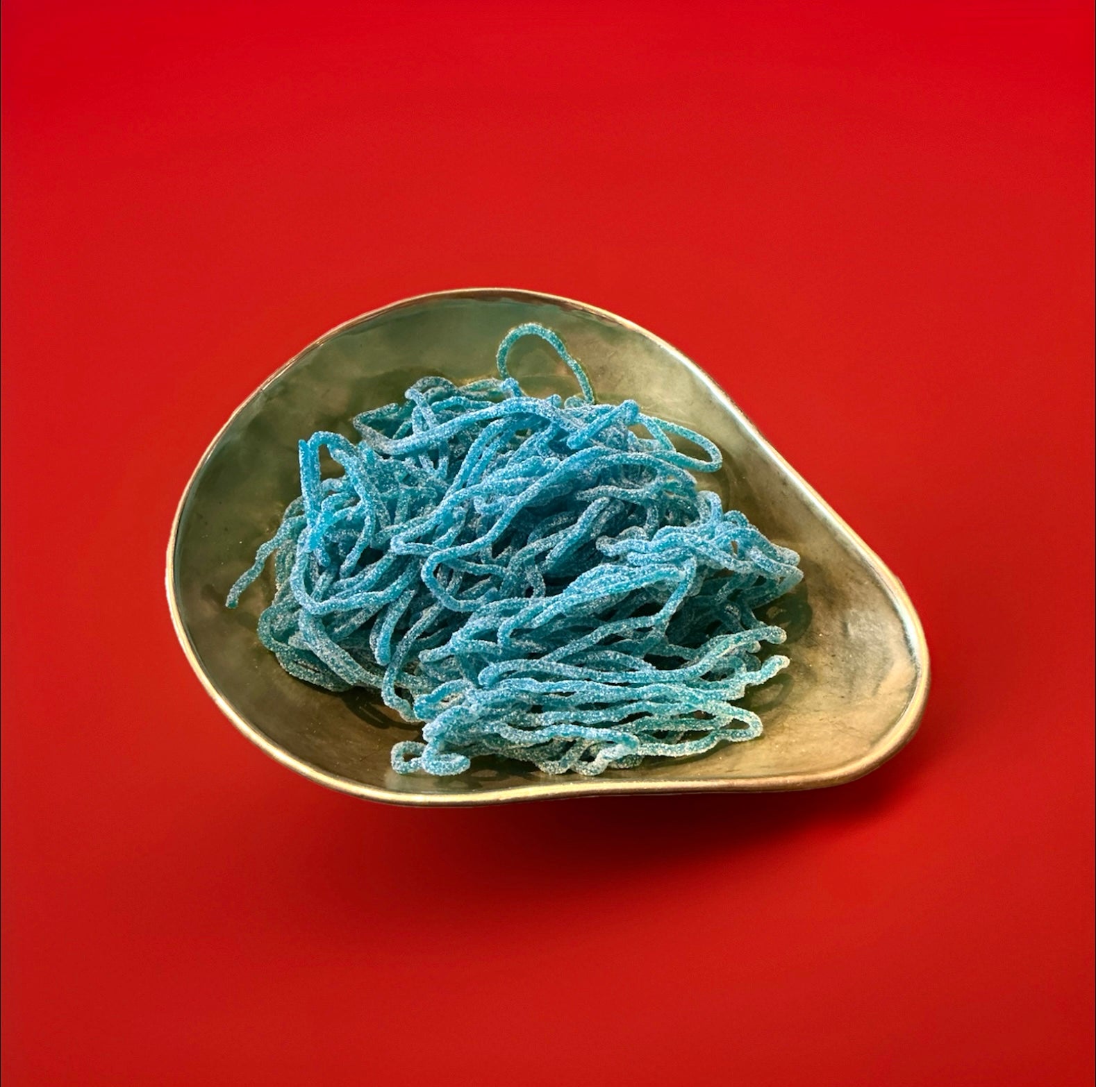 Blue raspberry flavoured sour laces in a gold bowl with a red background 