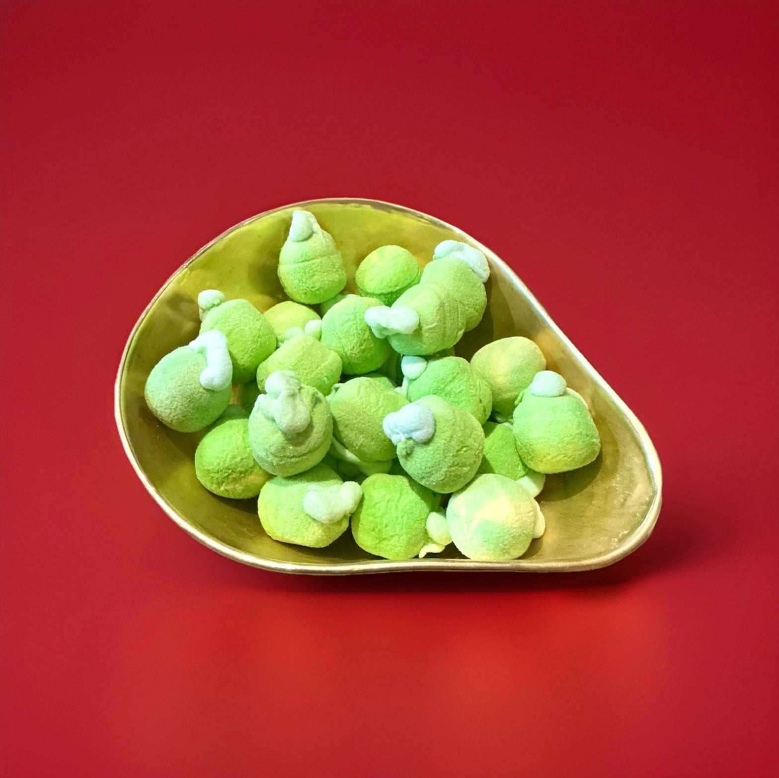 Large green coloured apple flavoured marshmallows with a jelly centre in a gold bowl with a red background 