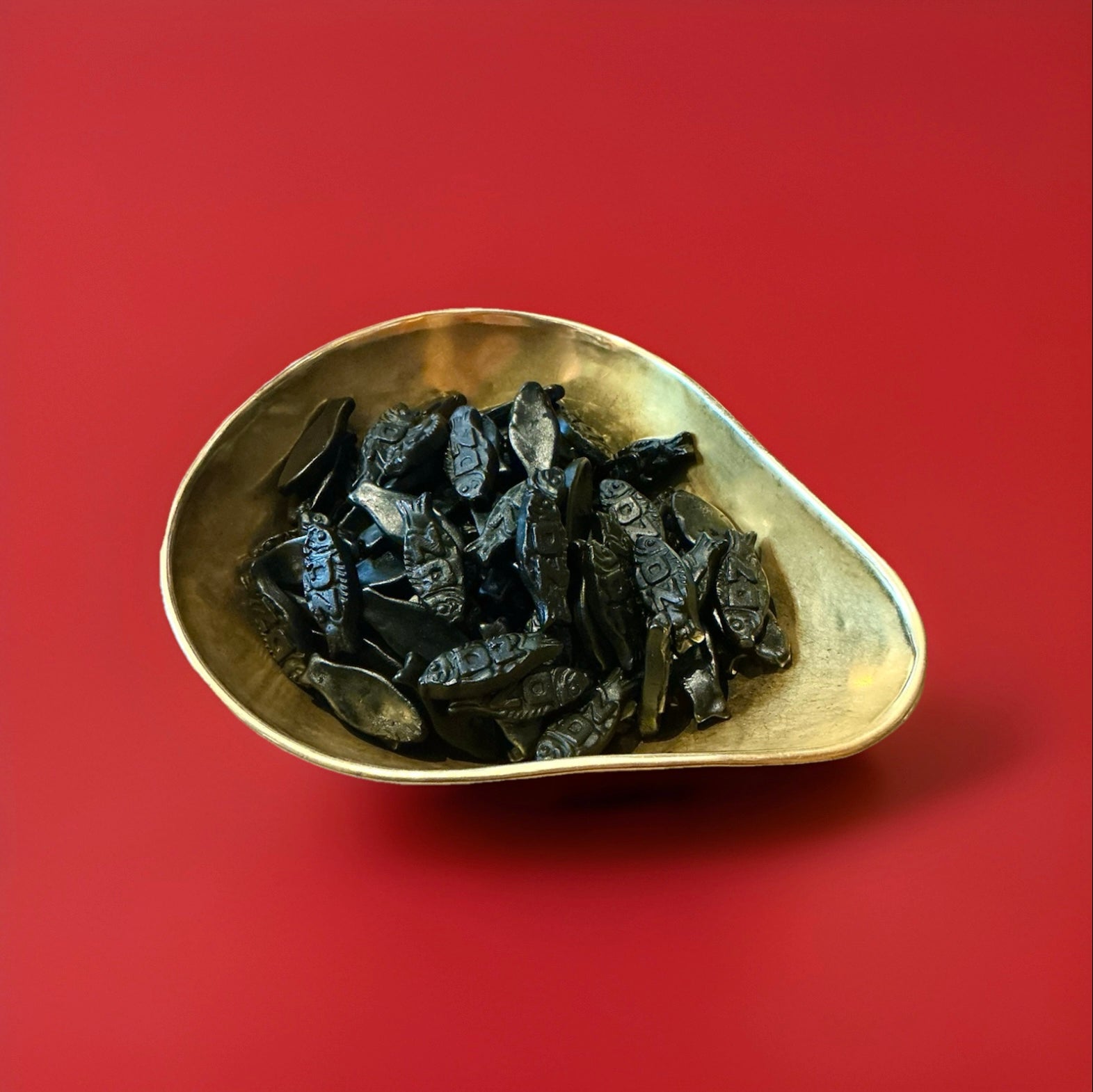 Dutch black double salted liquorice in the shape of a fish in a gold bowl on a red background 
