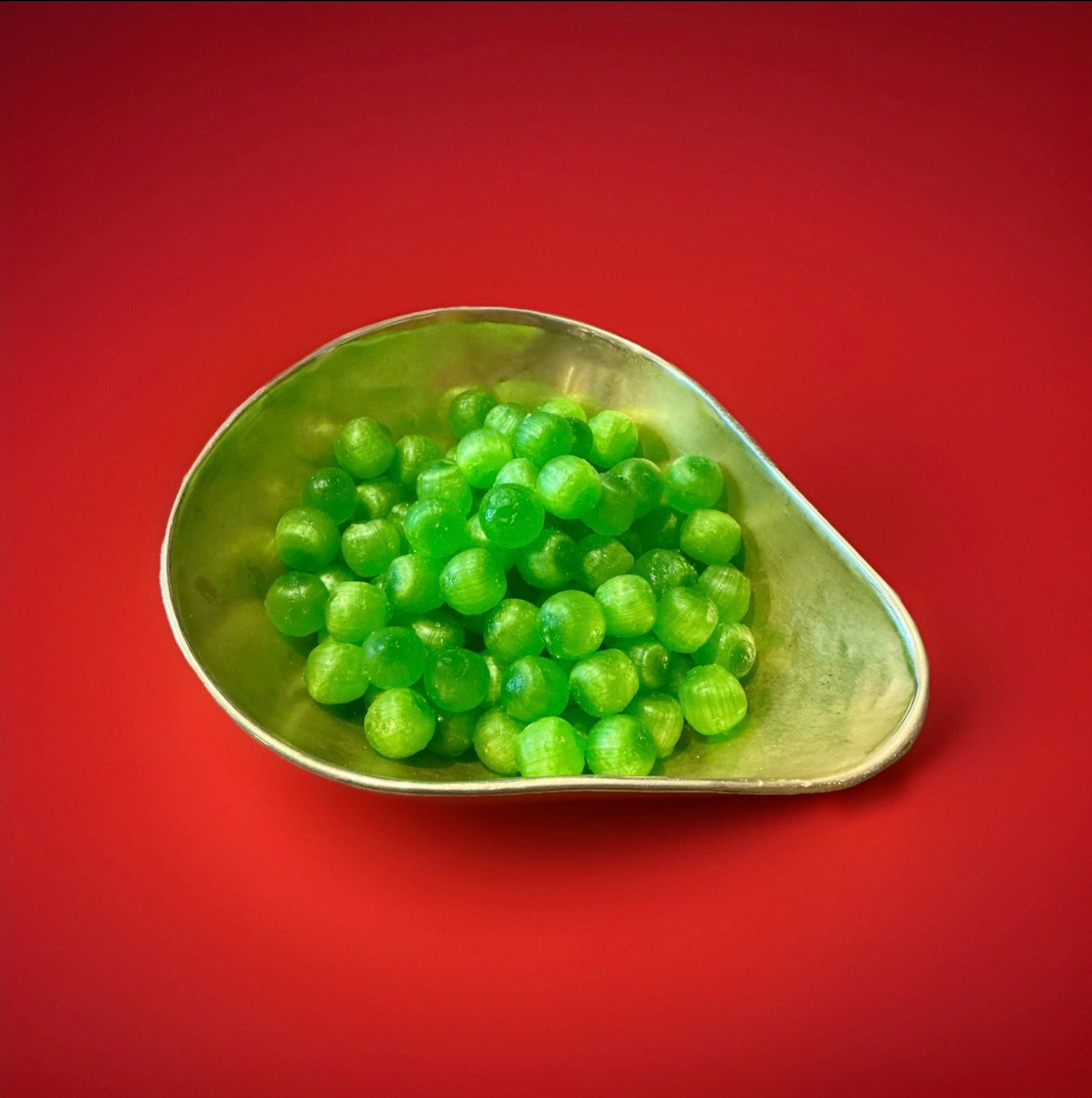 Green hard boiled sour apple flavoured sweets in a gold bowl on a red background 
