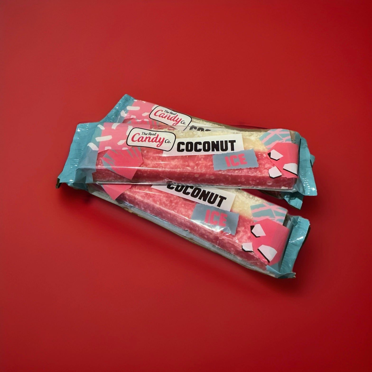 Pink and white coconut ice bar in a blue and pink wrapper on a red background 