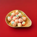Large peach coloured peach flavoured marshmallows with a jelly centre in a gold bowl on a red background 