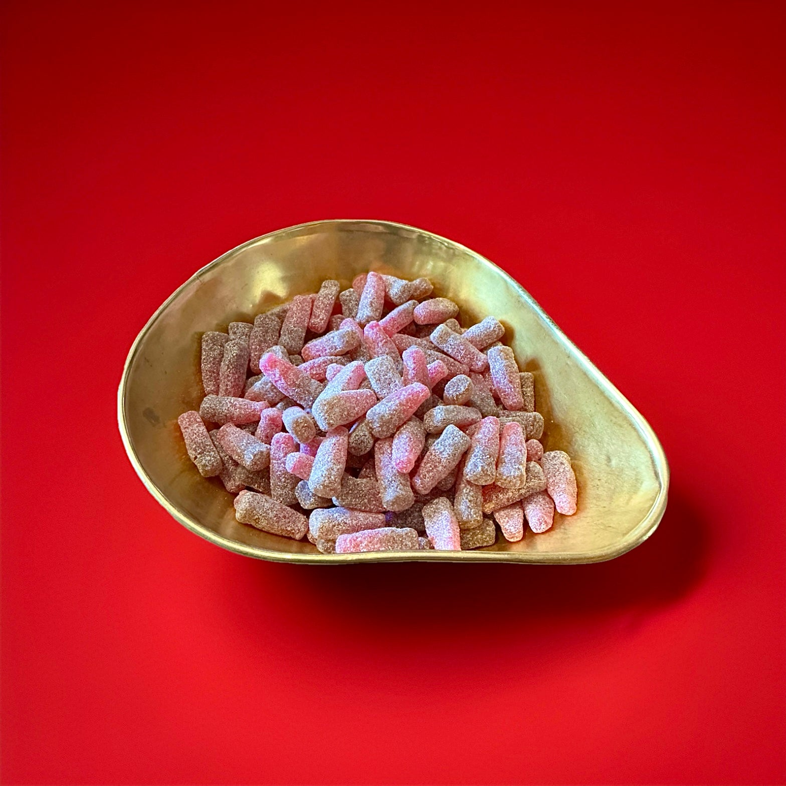 Red and brown bottle shaped jelly sweets with a fizzy sugar coating and cherry cola flavour in a gold bowl with a red background 