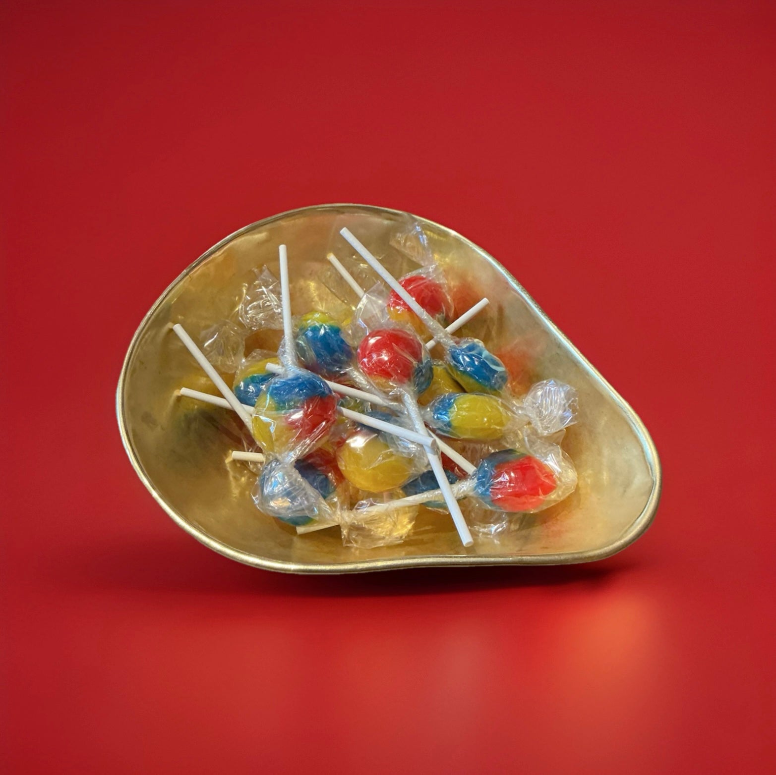 Individually wrapped hard boiled red yellow and blue tutti fruity lolly in a gold bowl on a red background 