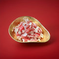Individually wrapped red and white striped boiled sweets with a clove flavour in a gold bowl on a red background 