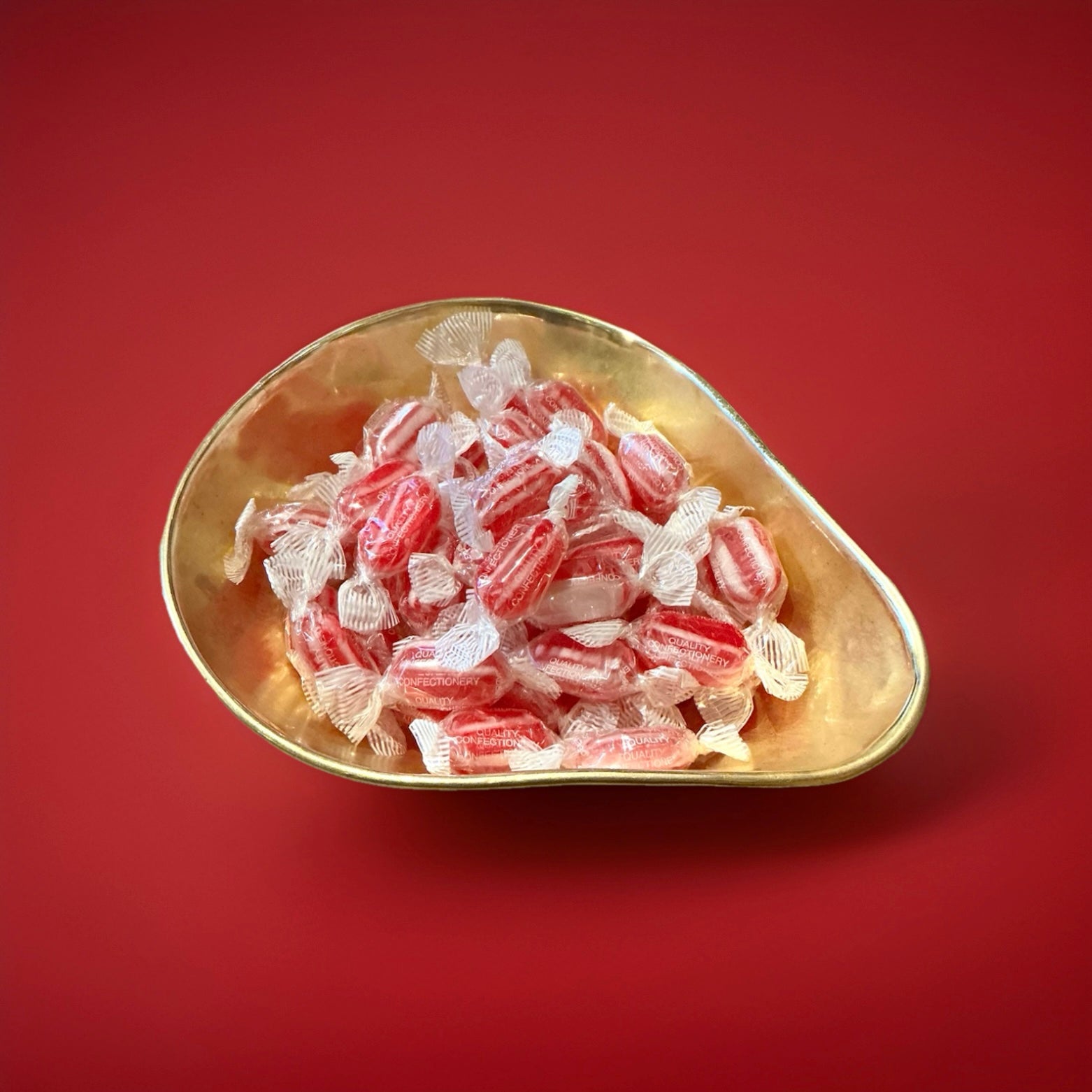 Individually wrapped red and white striped boiled sweets with a clove flavour in a gold bowl on a red background 