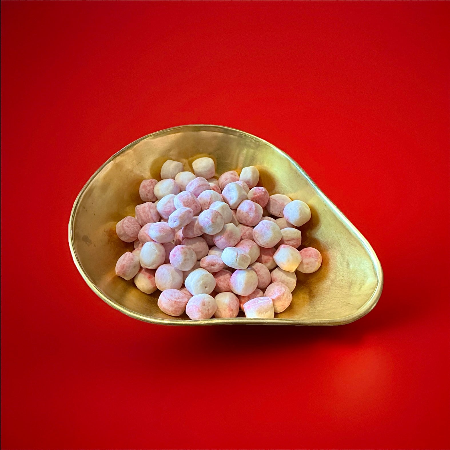 Ronny shaped pink and white coloured strawberry and cream flavoured Bon Bon’s in a gold bowl on a red background 