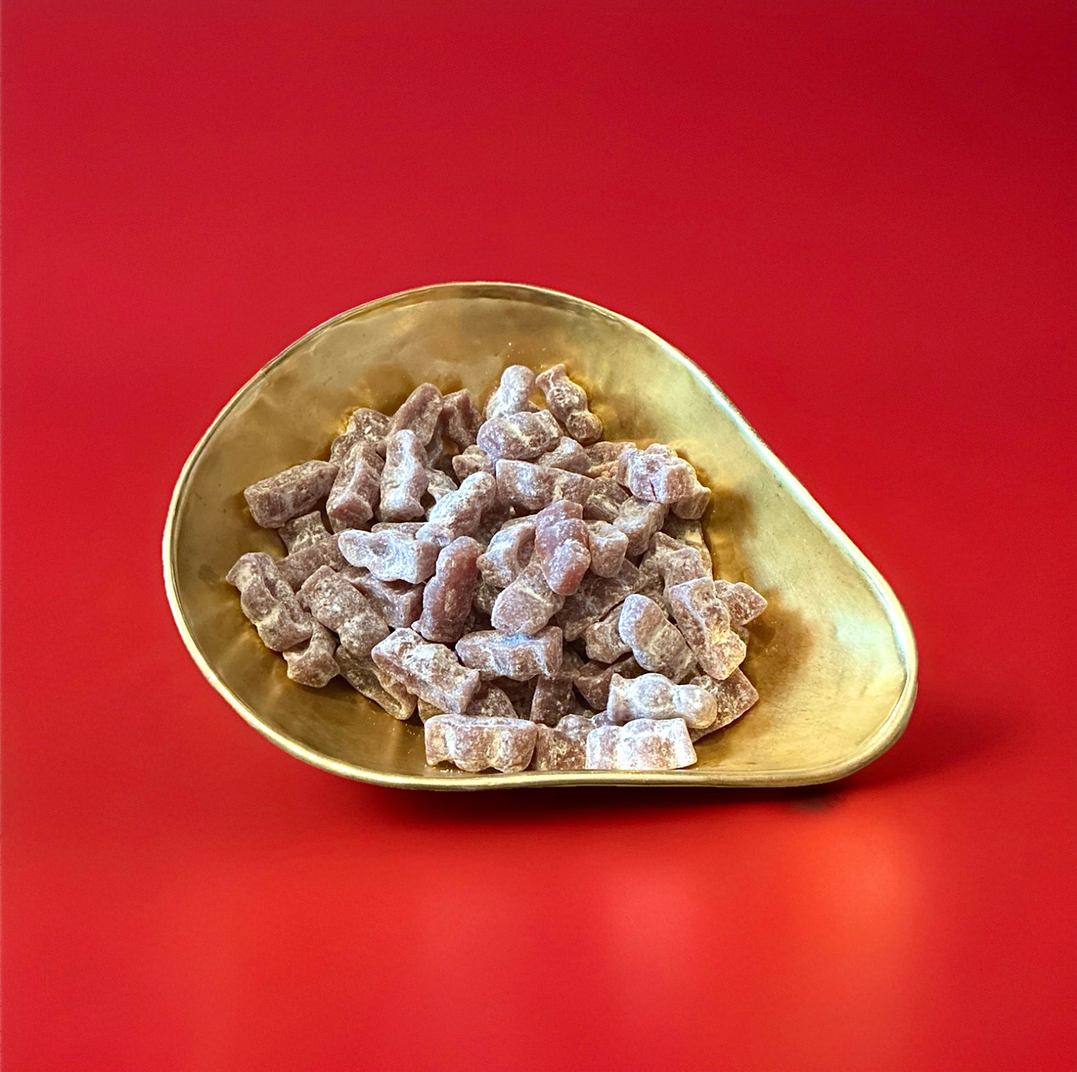 Purple Vimto flavoured jelly sweets in the traditional jelly baby shape in a gold bowl with a red background 