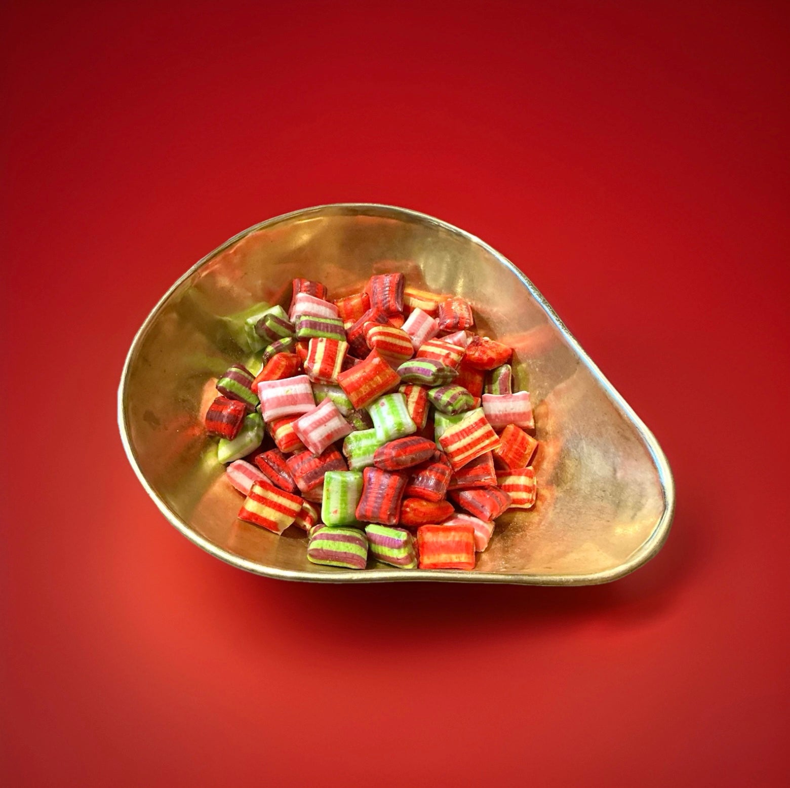 Multicoloured striped chocolate satins in a gold bowl on a red background 