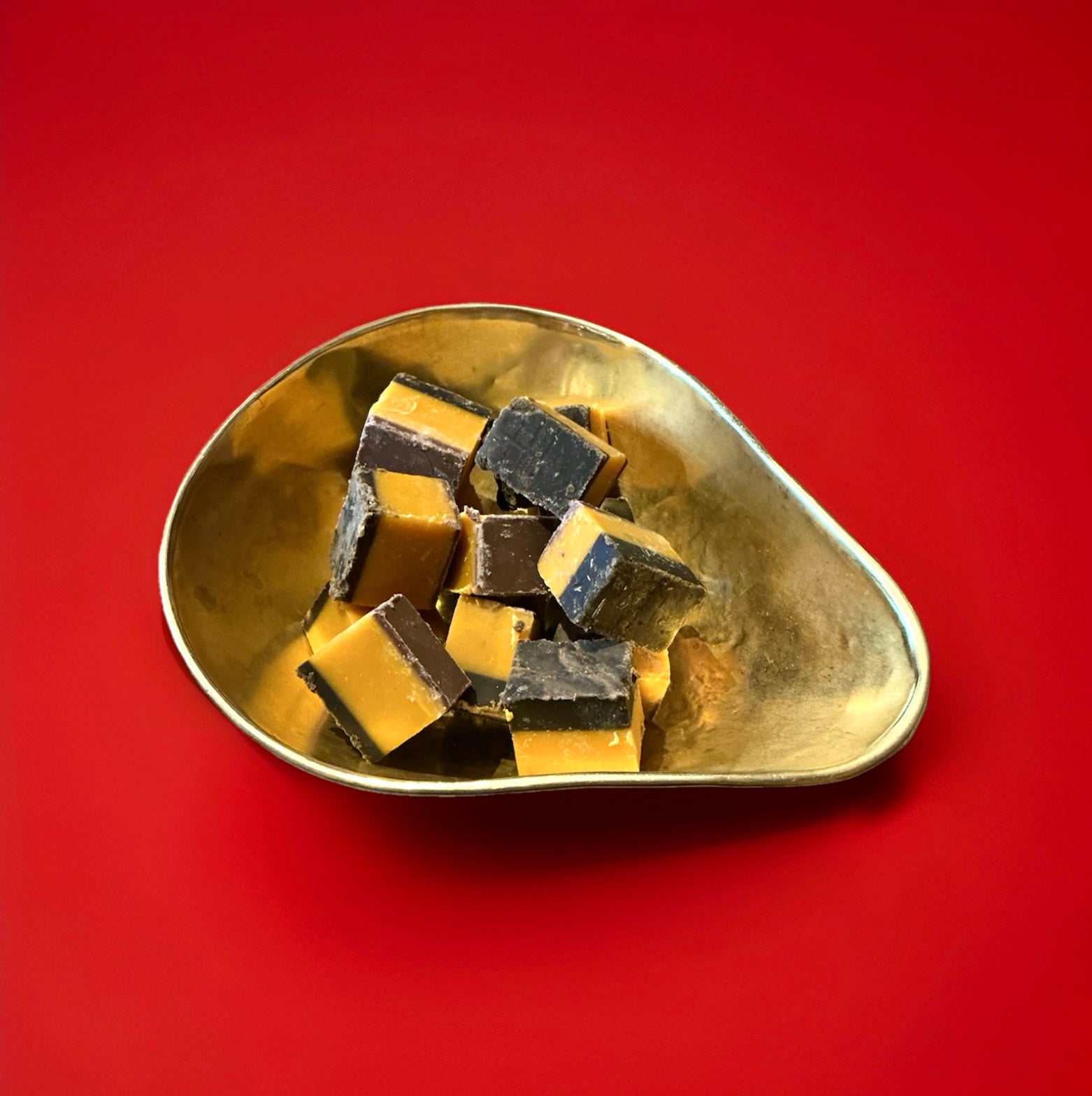 Large pieces of Daim bar flavoured fudge in a gold bowl with a red background 