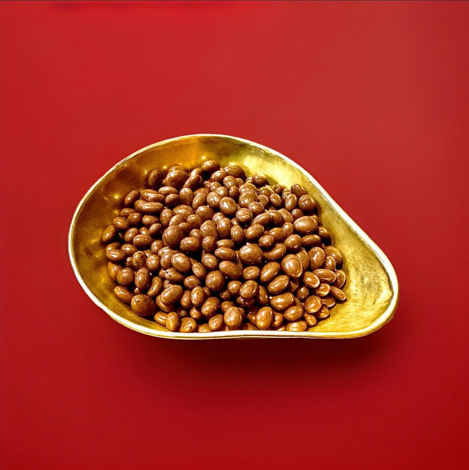 Milk chocolate covered raisins in a gold bowl on a red background 