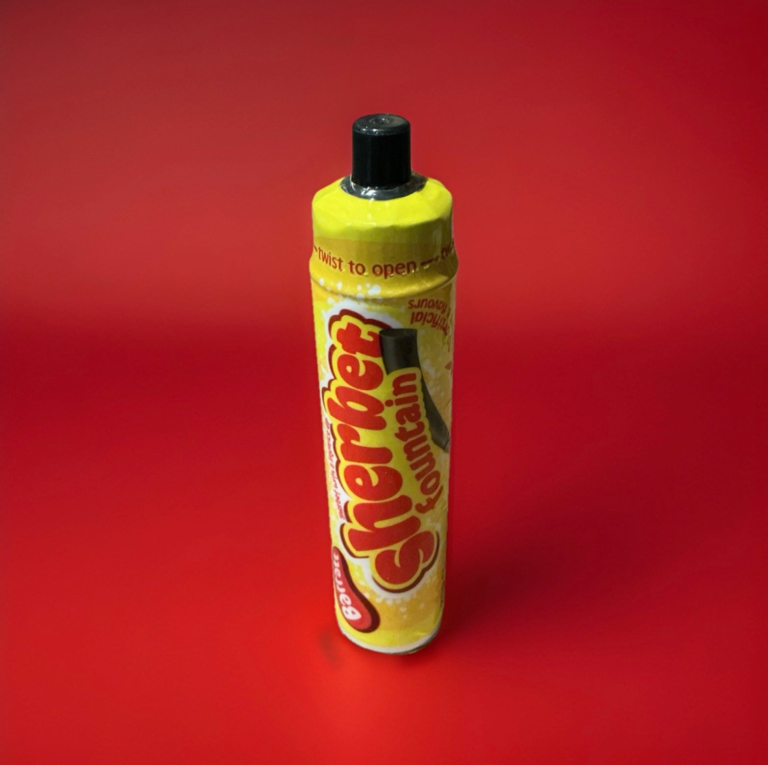 Yellow plastic tube with a black top filled with sherbet and a black liquorice stick on a red background 