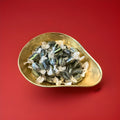 Individually wrapped liquorice and lime flavoured black and green striped sweets in a gold bowl on a red background 